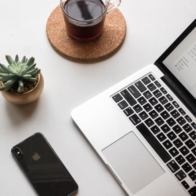 A laptop, phone, cup of coffee and succulent plant on a white desk with a webpage open on the laptop screen